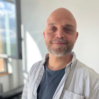 Ein Mann mit Master of Science und zertifizierter Sachverständiger lächelt vor einem hellen Hintergrund.